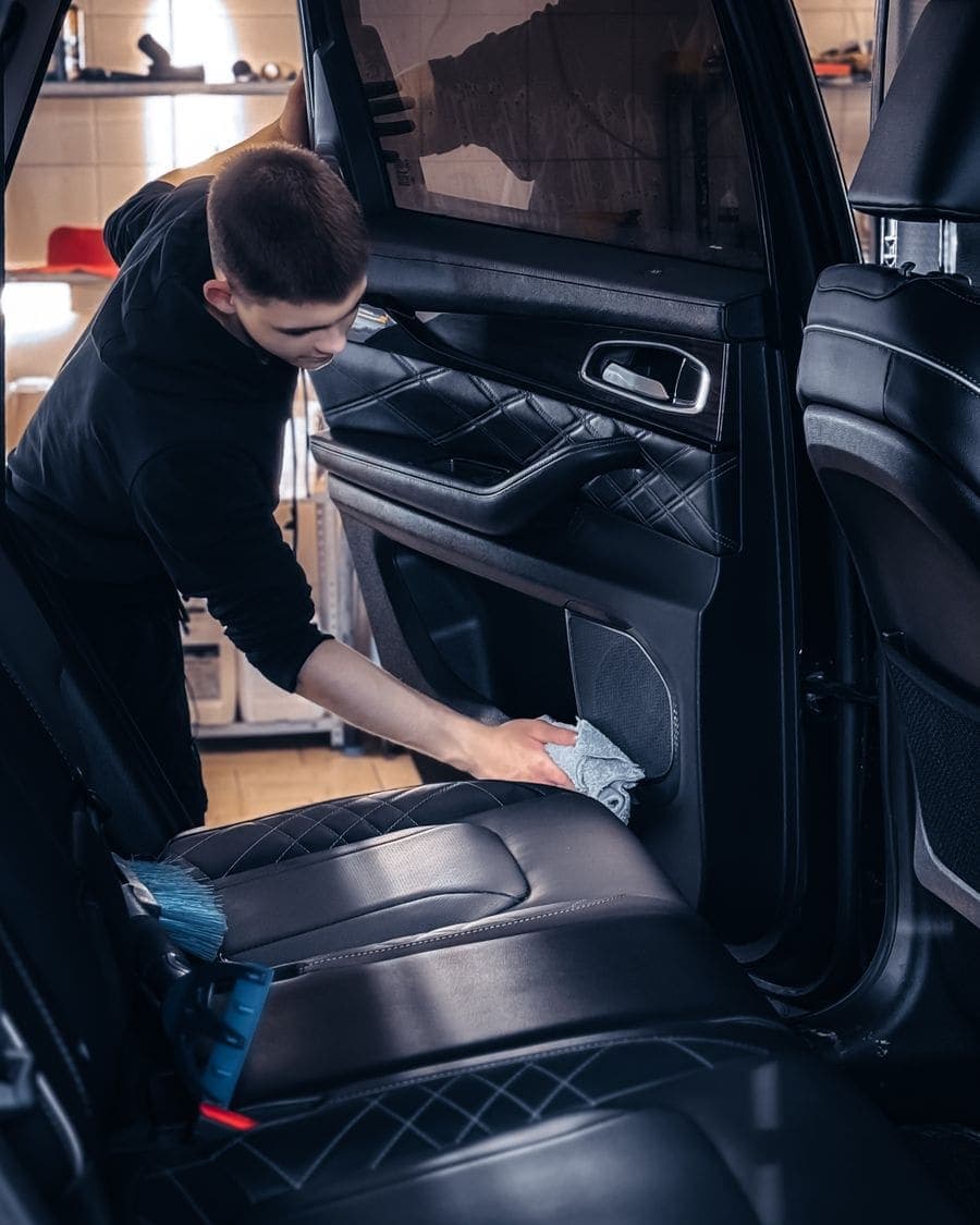 Persona limpiando con un paño la puerta y los asientos por dentro del carro